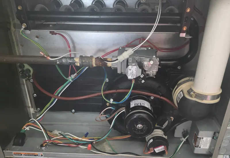 Open gas furnace cabinet showing the blower motor, gas valve, and control wiring during a furnace service call